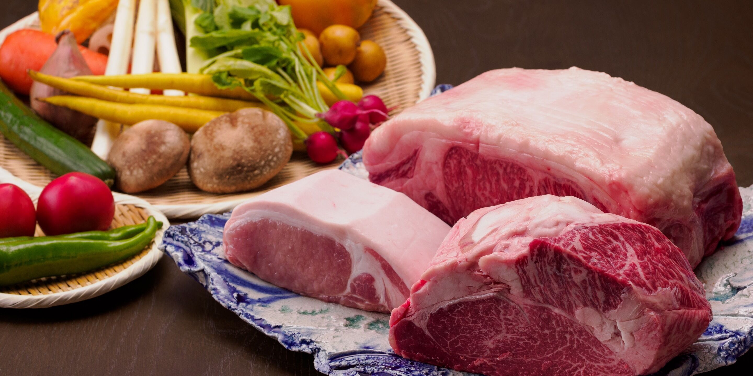Une variété de légumes frais et deux morceaux de viande sont disposés sur une table en bois.