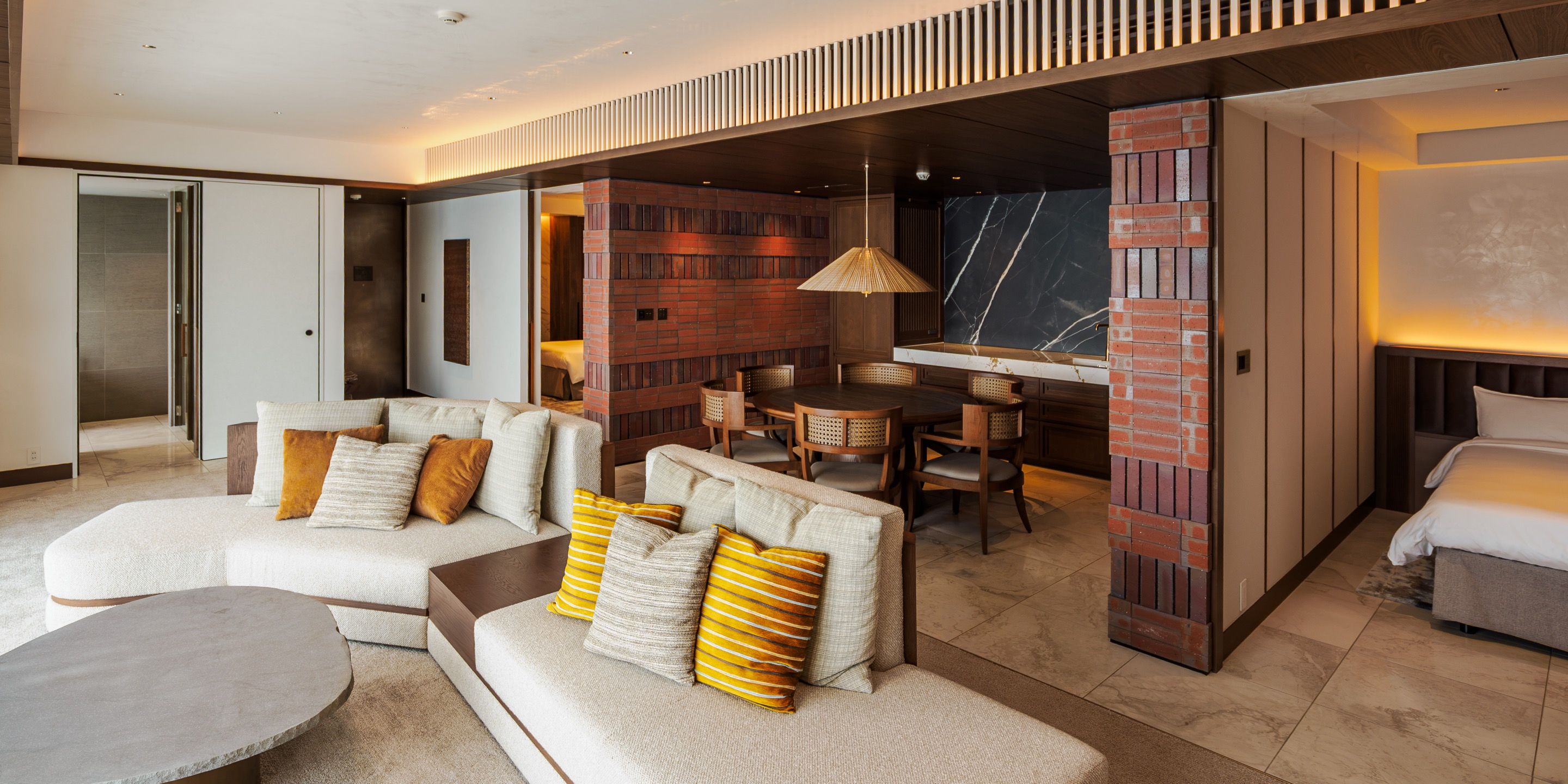 Una habitación de hotel moderna con un sofá seccional, una zona de comedor y una área de descanso separada.