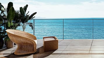 Una silla de mimbre y un reposapiés sobre una terraza con baldosas y vista al océano.