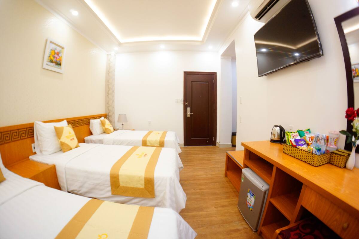 A hotel room with two beds, a desk with a refrigerator, a television, and a door leading to another room.