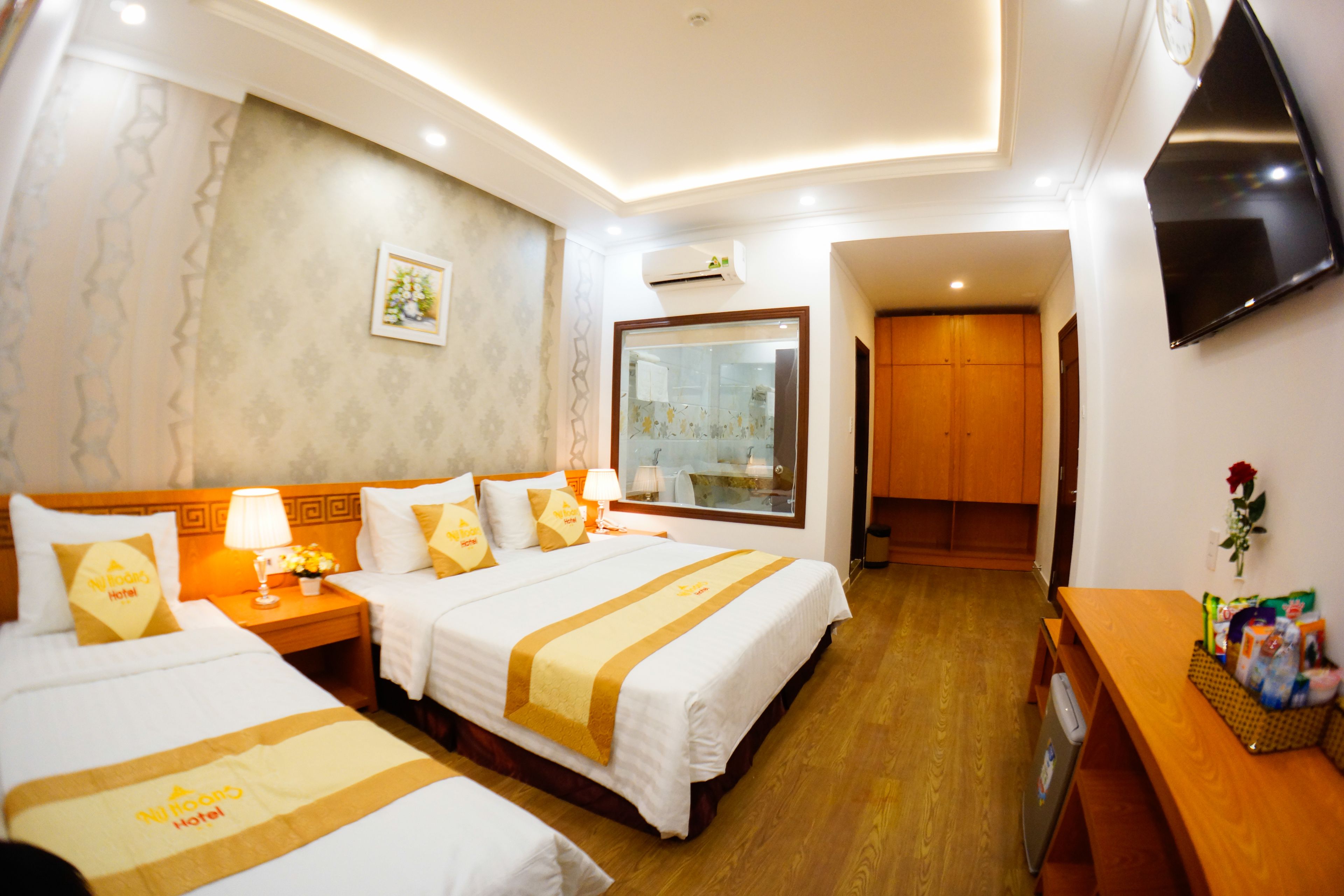 A hotel room with two beds, a wooden desk, a TV, and a bathroom door.
