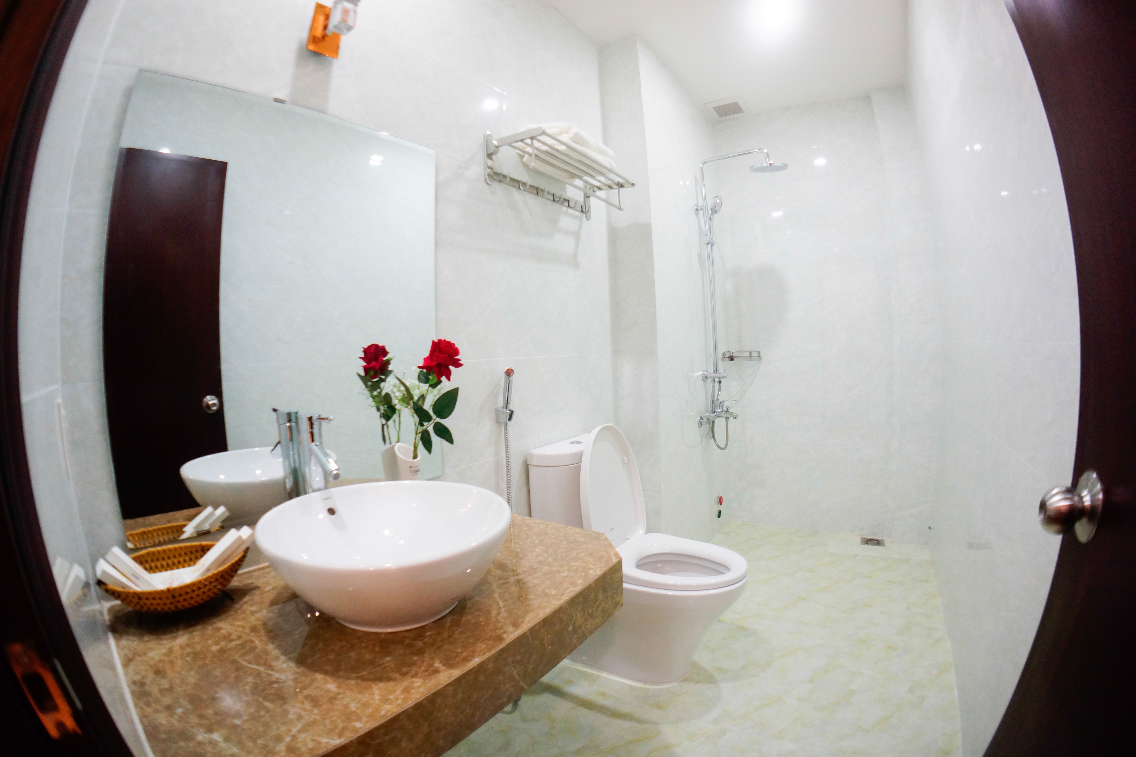 A modern bathroom with a large mirror, a white sink, a toilet, and a shower area.