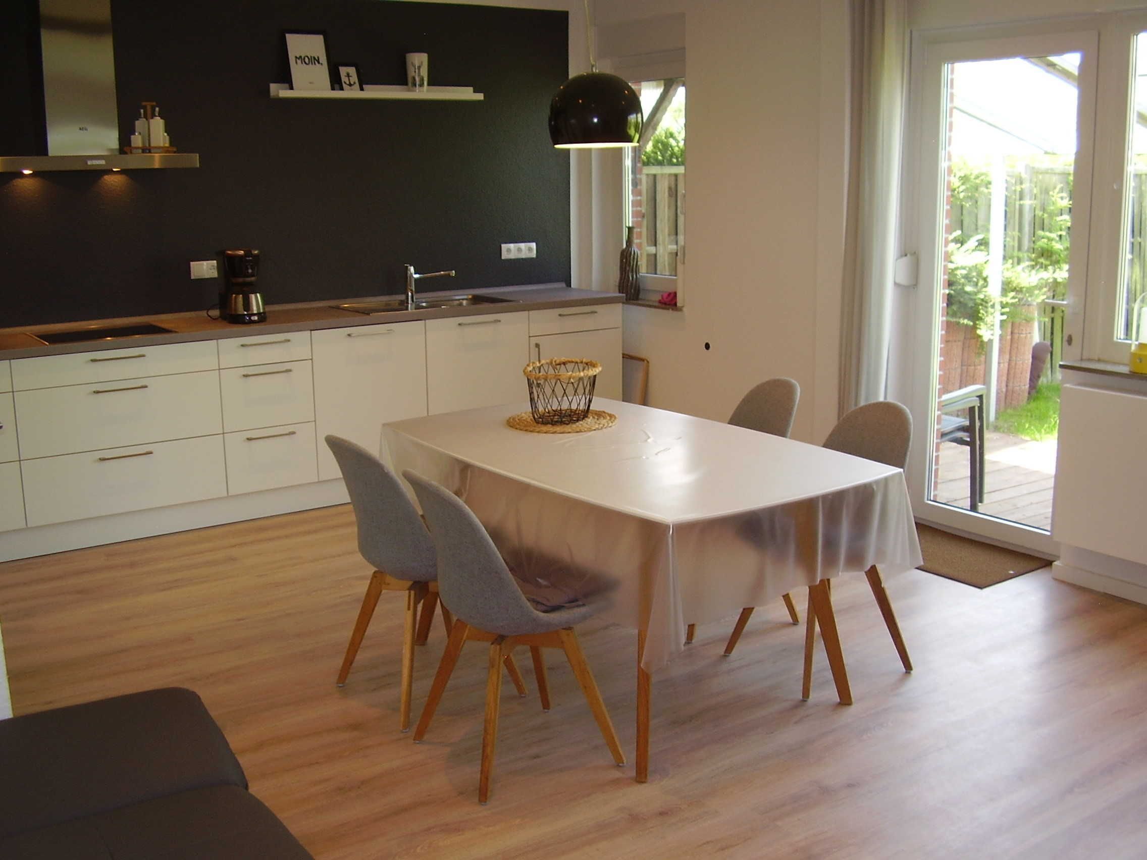 A modern kitchen with white cabinets, a black pendant light, and a dining area with a table and chairs.