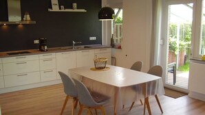 A modern kitchen with white cabinets, a black pendant light, and a dining area with a table and chairs. - Vacation home in Dornumersiel 20-138a - 200-138a (Dornum)