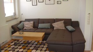 A modern living room with a brown sectional sofa, a wooden coffee table, and a patterned rug. - Vacation home in Dornumersiel 20-138a - 200-138a (Dornum)