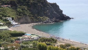 Vista costera con playa, acantilados rocosos y un edificio de techo verde.