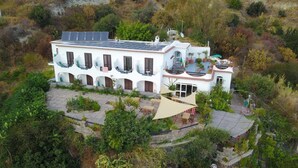 Una villa blanca con varios balcones, paneles solares y un patio con mobiliario exterior.