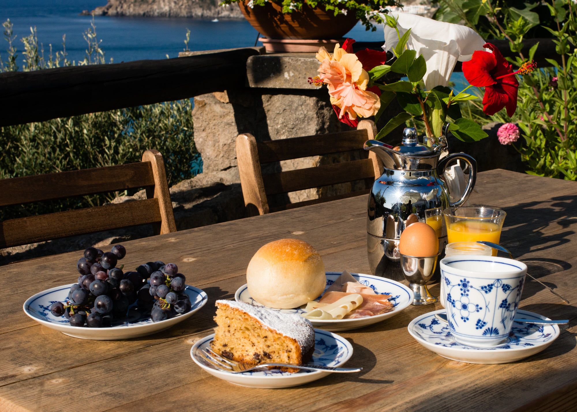 A breakfast table with plates of food, a teapot, and a cup of orange juice.