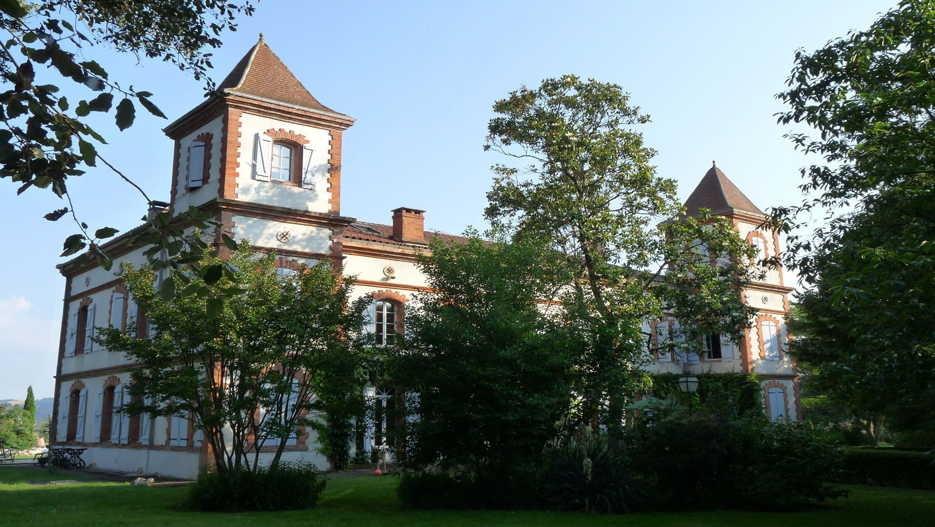 A large, historic building with two prominent towers, surrounded by lush greenery.