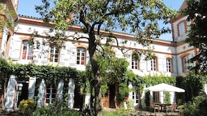 Un edificio tradicional con patio, que presenta un árbol grande, una zona de estar techada y fachada de ladrillo.