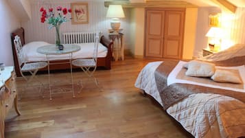 A cozy bedroom with a bed, a small table with chairs, a radiator, and a lamp.