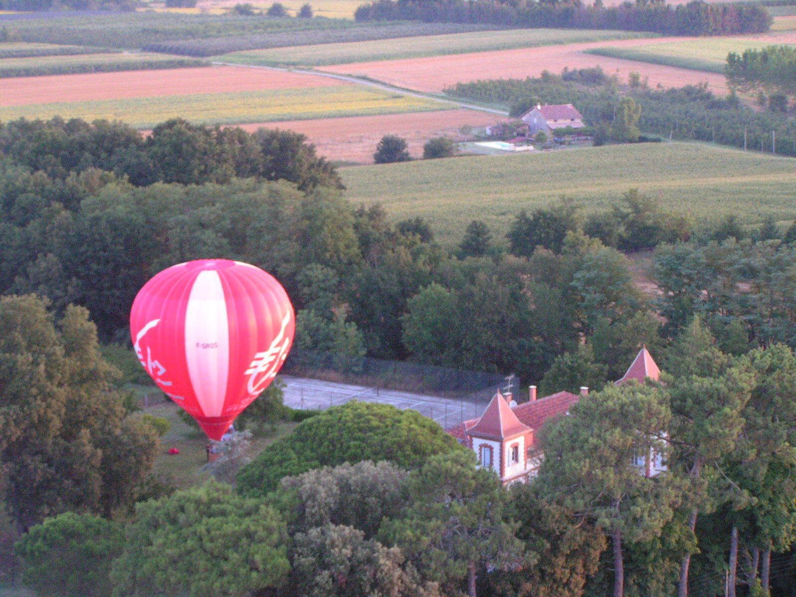 Eine rote Heißluftballon über einer ländlichen Landschaft mit Feldern und einem kleinen Haus.