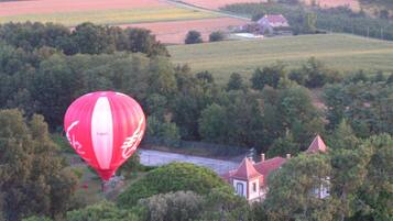 A red hot air balloon over a rural landscape with fields and a small house.