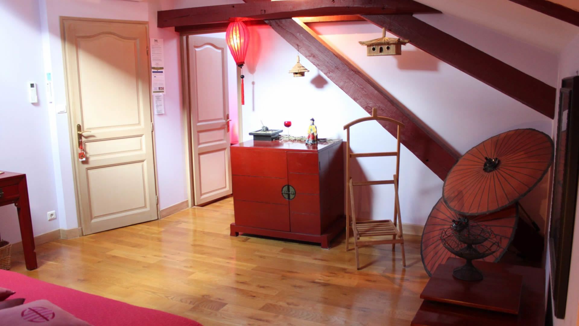 Ein Zimmer mit Holzboden, einem roten Schminktisch, einer Holzleiter, einem roten Laternenlicht und einem traditionellen Regenschirm.