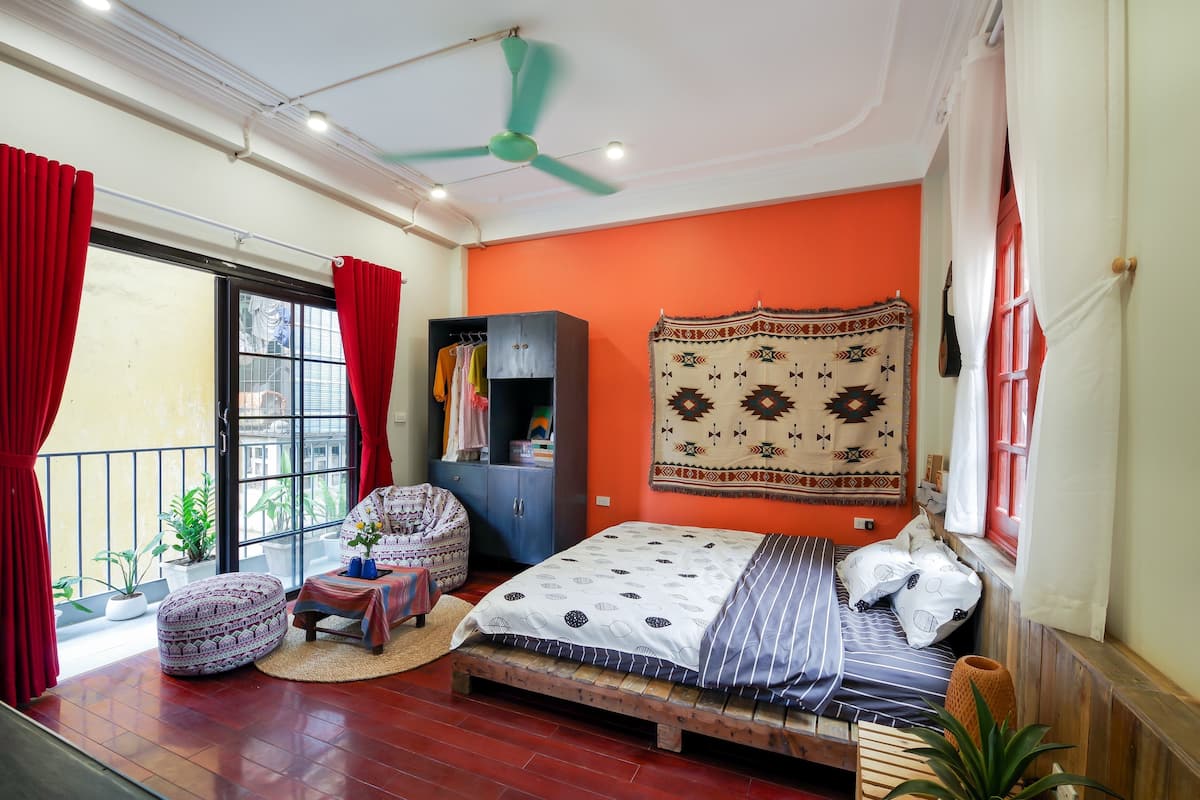 A bedroom with a bed, a wardrobe, a window with curtains, a ceiling fan, and a view of the outside.