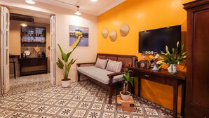 Uma sala de estar com um sofá, uma televisão, uma planta em vaso e um painel decorativo.