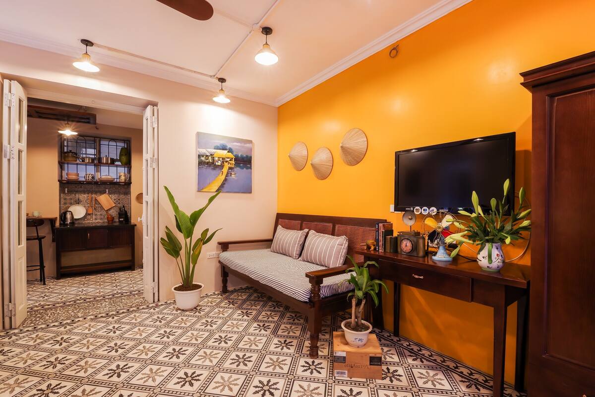A living room with a sofa, a television, a potted plant, and a decorative wall.