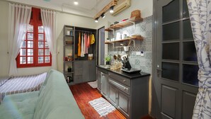 Um espaço compacto com cozinha compacta, cama com roupa de cama listrada e janela com persianas vermelhas.