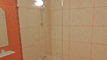 Une douche fermée par des parois en verre, dotée d’un pommeau de douche à main, d’un lavabo blanc et d’un miroir au-dessus du lavabo.