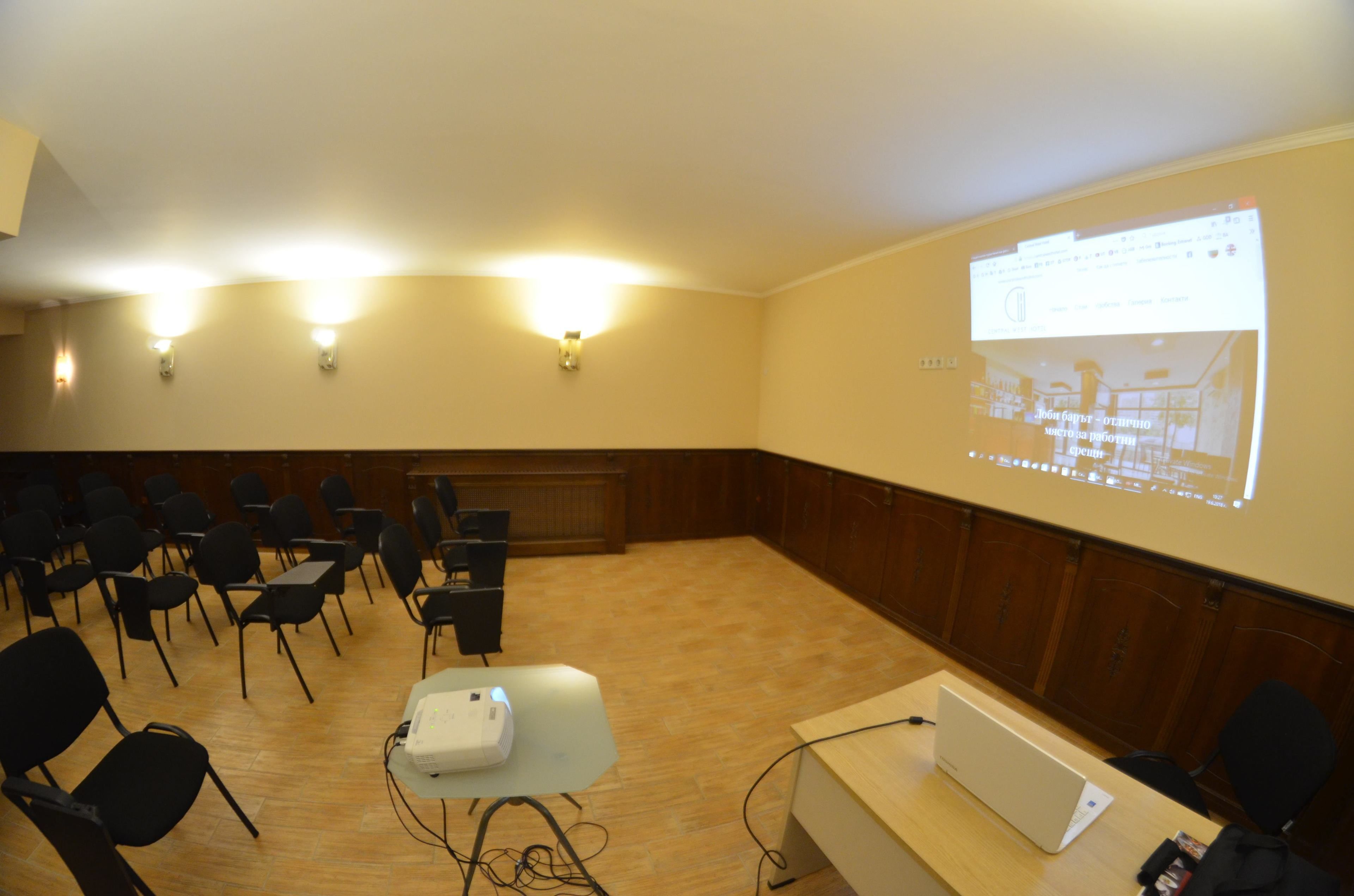 Une salle de conférence dotée d’un grand écran de projection, de panneaux muraux en bois et de chaises noires disposées en rangées.