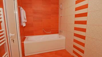 A bathroom with a white bathtub, orange and beige tiles, and a towel rack.