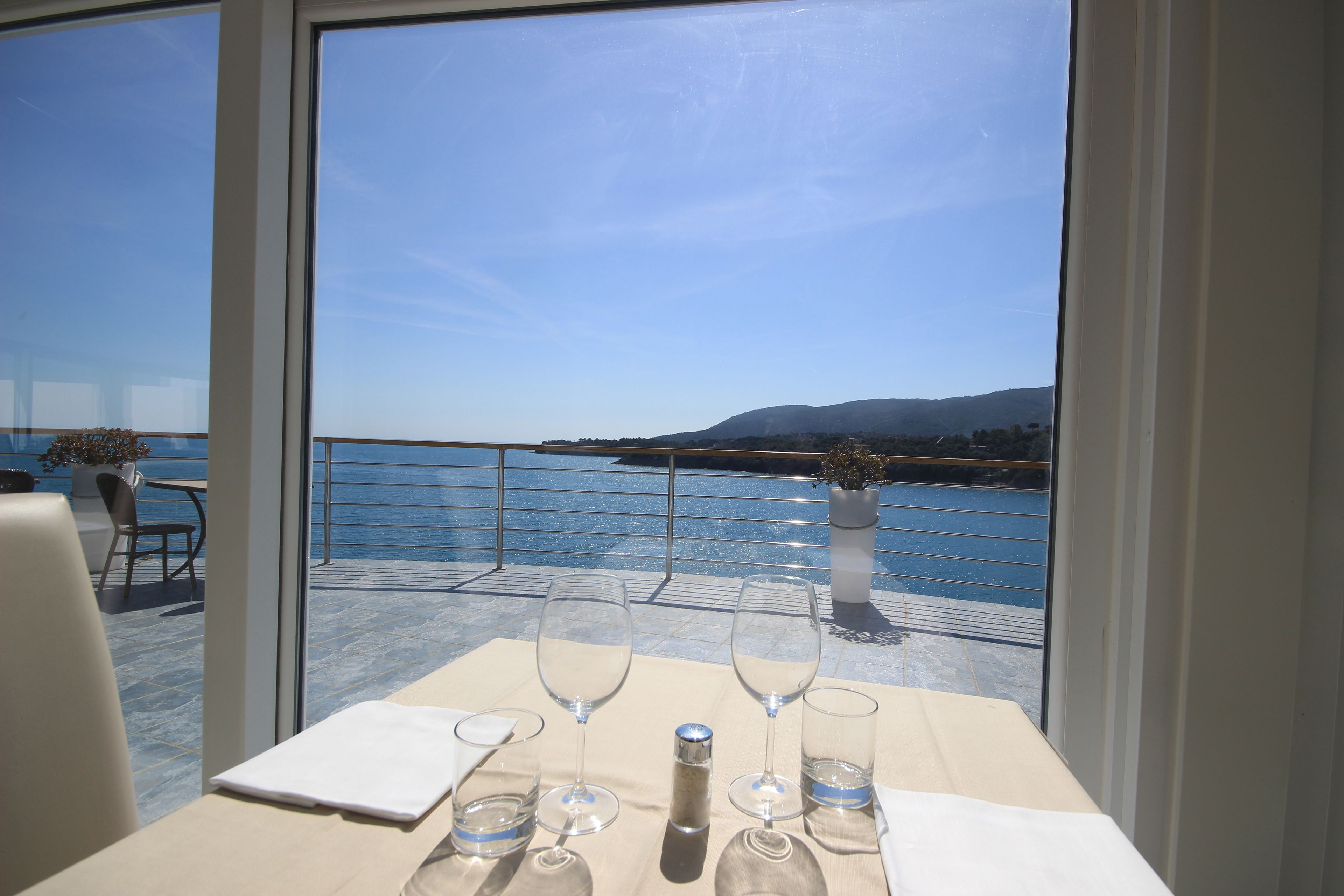 A table with wine glasses and a bottle, overlooking a body of water with a mountain in the distance.