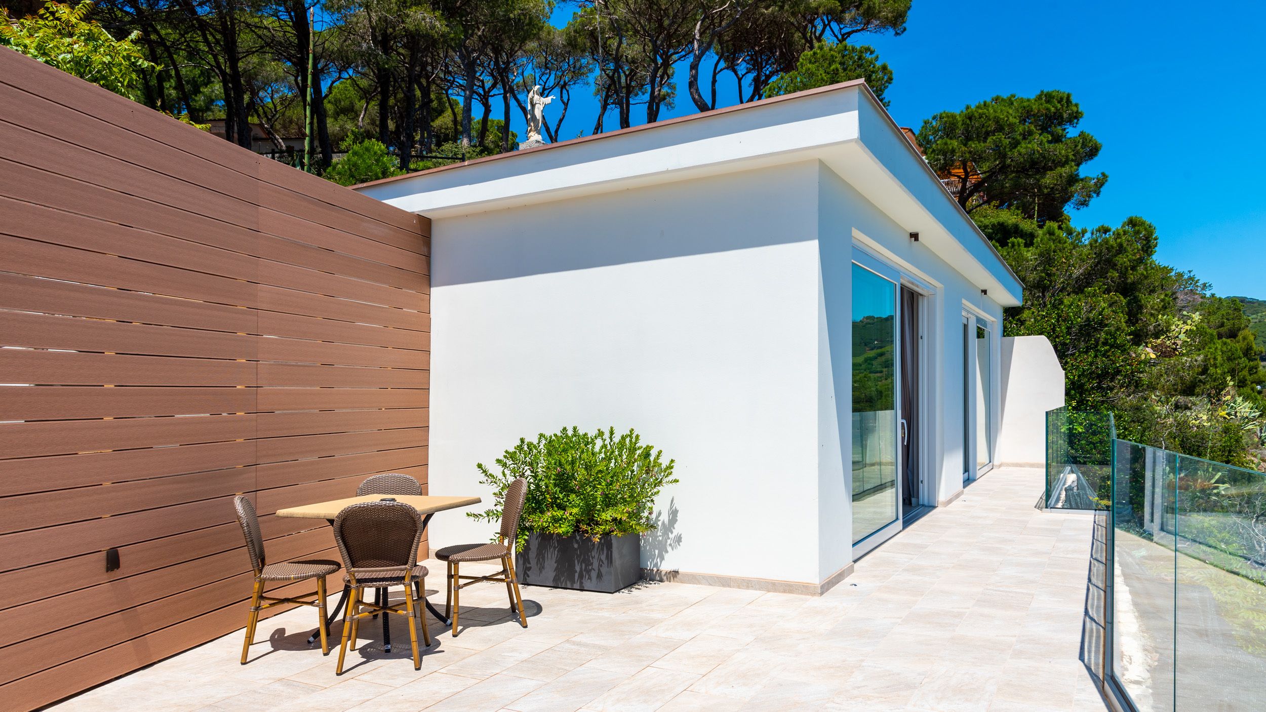 A modern outdoor patio with a wooden wall, a table with wicker chairs, and a potted plant.