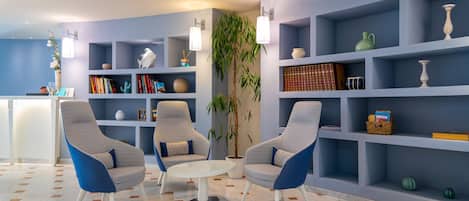 Un área de descanso moderna con tres sillones, una mesa redonda y una estantería llena de libros y objetos decorativos.