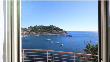 Une vue sur la côte, prise depuis un balcon, avec un ciel dégagé, une petite île parsemée de bâtiments et plusieurs bateaux sur l’eau.