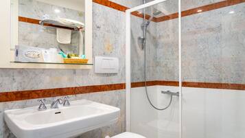 A bathroom with a white sink, a toilet, a glass-enclosed shower, and a marble-tiled wall with orange accents.