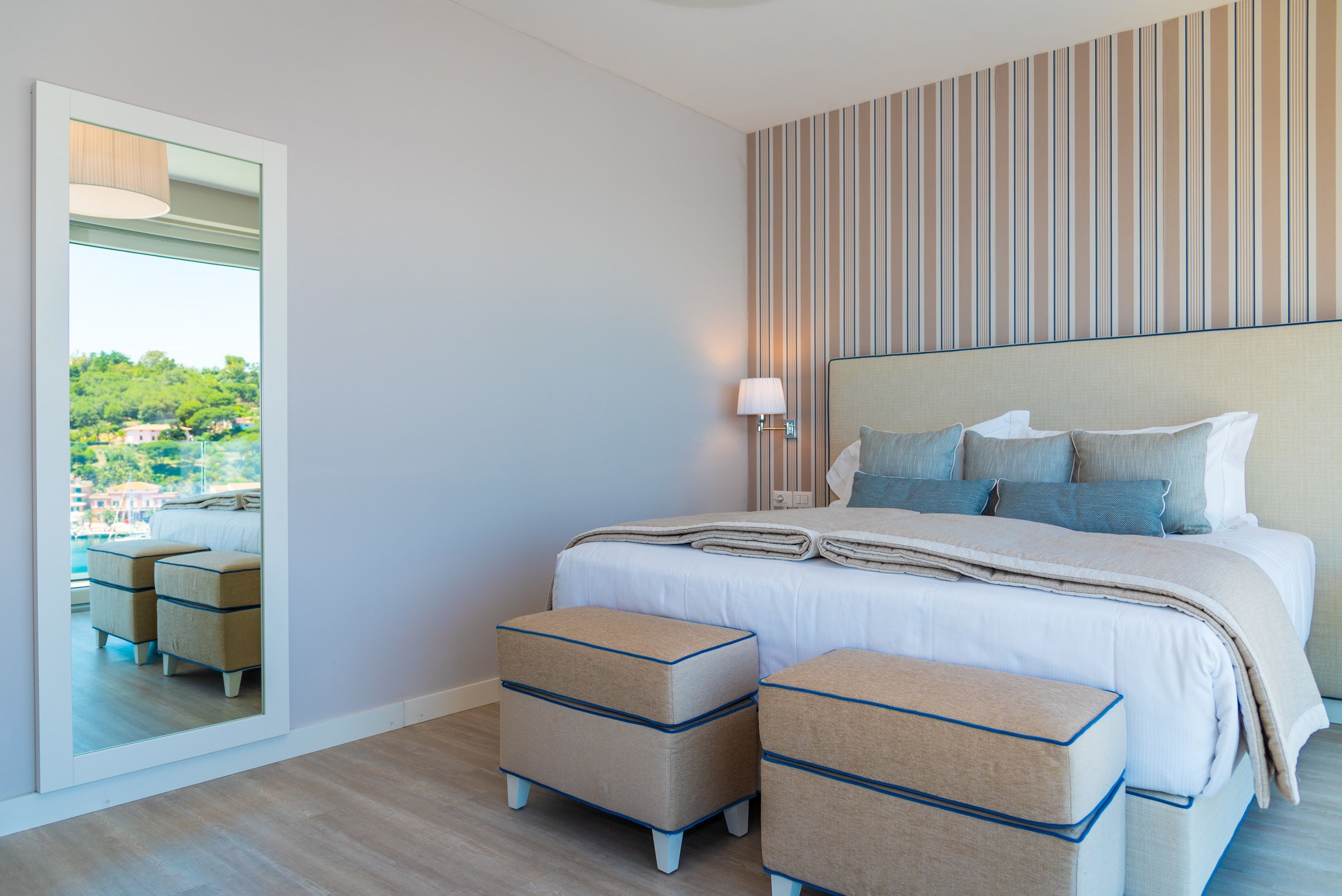 Un dormitorio moderno con una cama grande, dos mesitas de noche, un espejo y vistas a una piscina y zonas verdes.