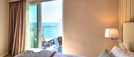 A hotel room with a bed, a chair, a lamp, and a view of the sea through a sliding door.