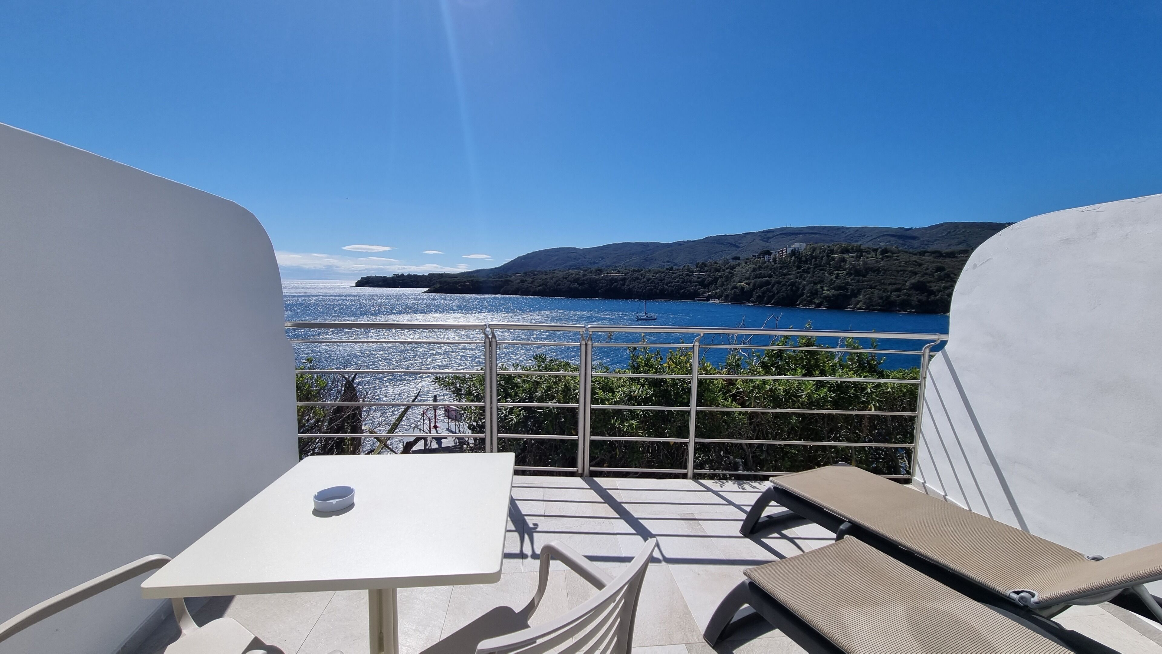 Un balcón con mesa y sillas, con vistas a un cuerpo de agua y un paisaje montañoso.
