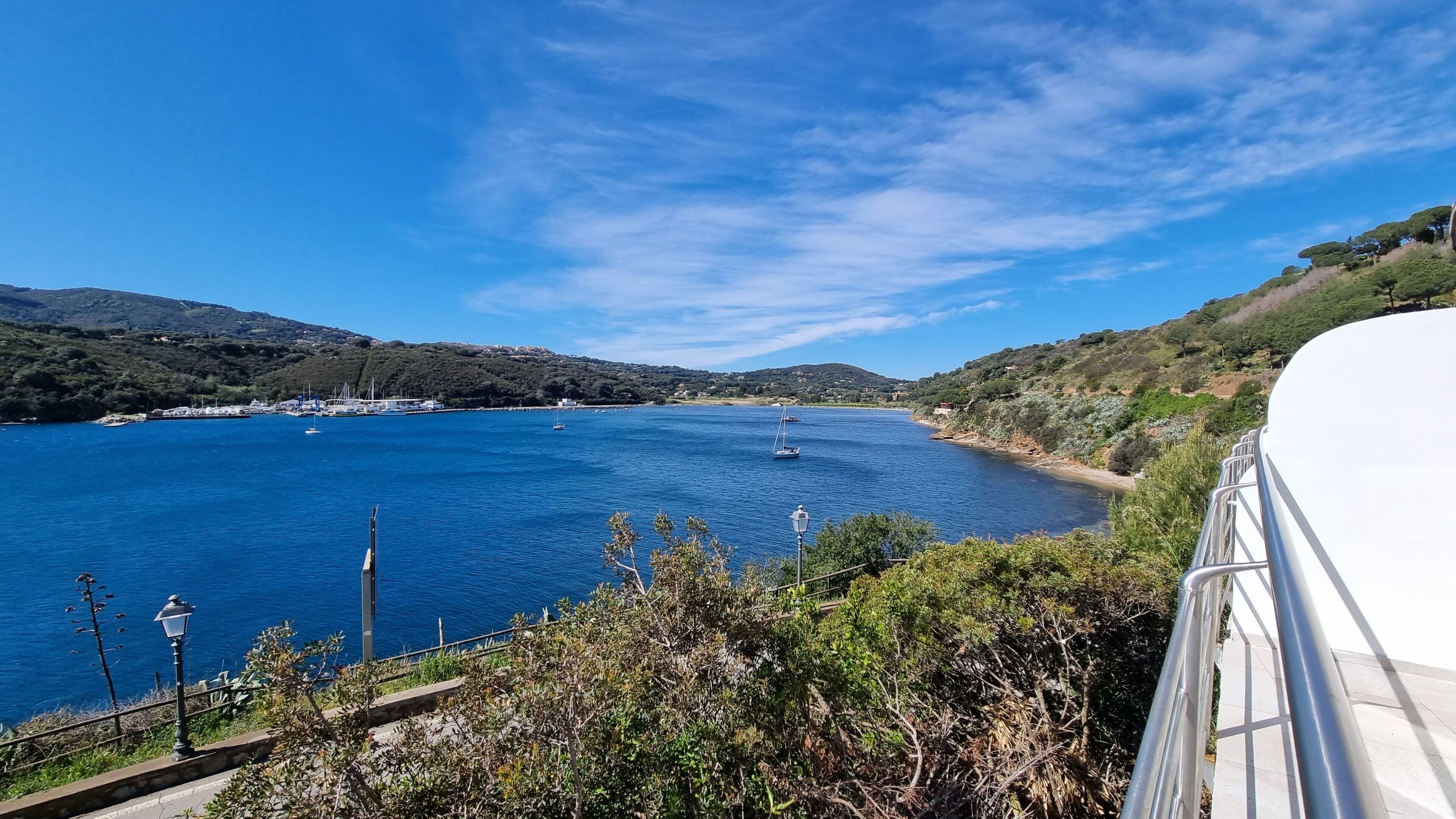 Küstensicht mit blauem Meer, Booten und hügeliger Landschaft.