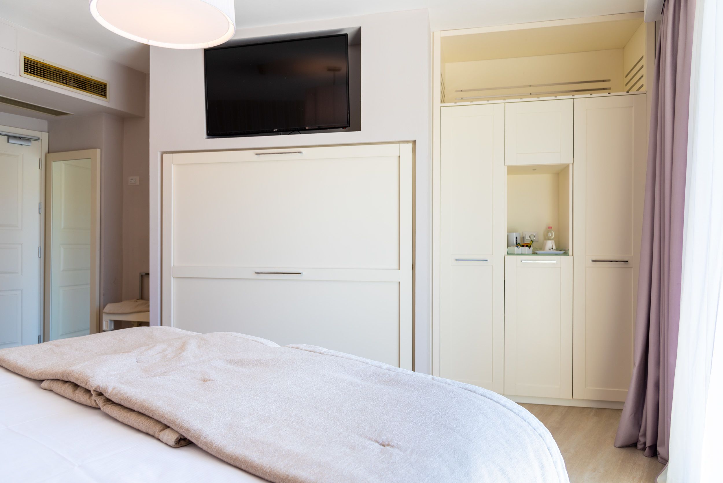 A bedroom with a bed, a television mounted on the wall, and a wardrobe with a mirror.