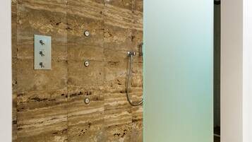 Un baño con pared de piedra, ducha y puerta de vidrio satinado.
