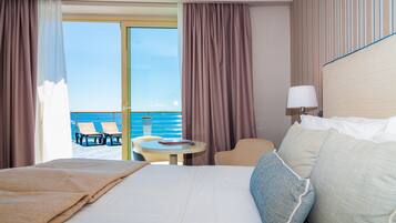 A hotel room with a bed, a small table, a chair, and a view of the sea.