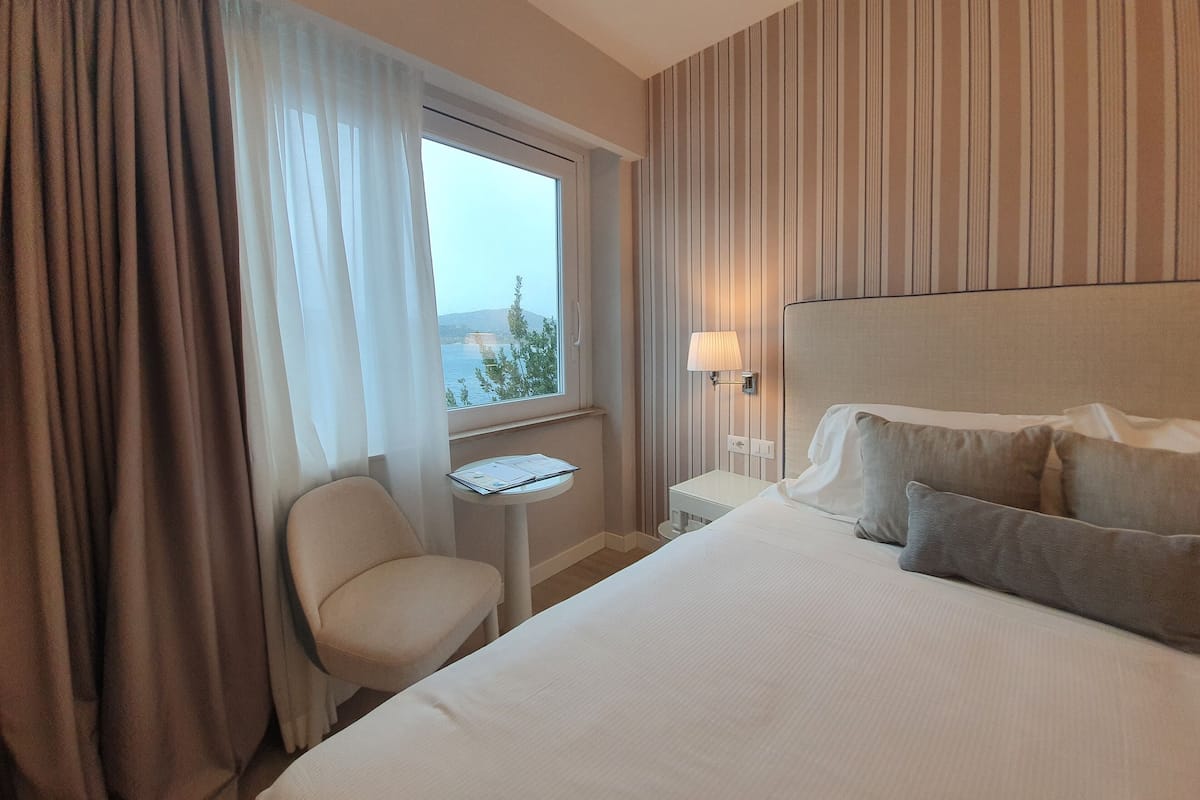 Habitació d'hotel amb llit, una cadira, una taula petita i una finestra amb cortines.