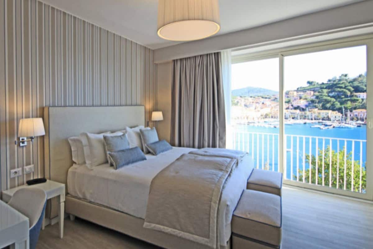 Habitació d'hotel amb llit, làmpades de nit, escriptori i vista a una població costanera.