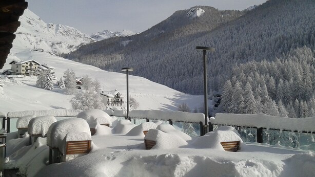 Paisaje nevado de montaña con un chalet y una terraza de madera con bancos.