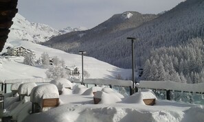 Een besneeuwd berglandschap met een chalet en een houten terras met banken.