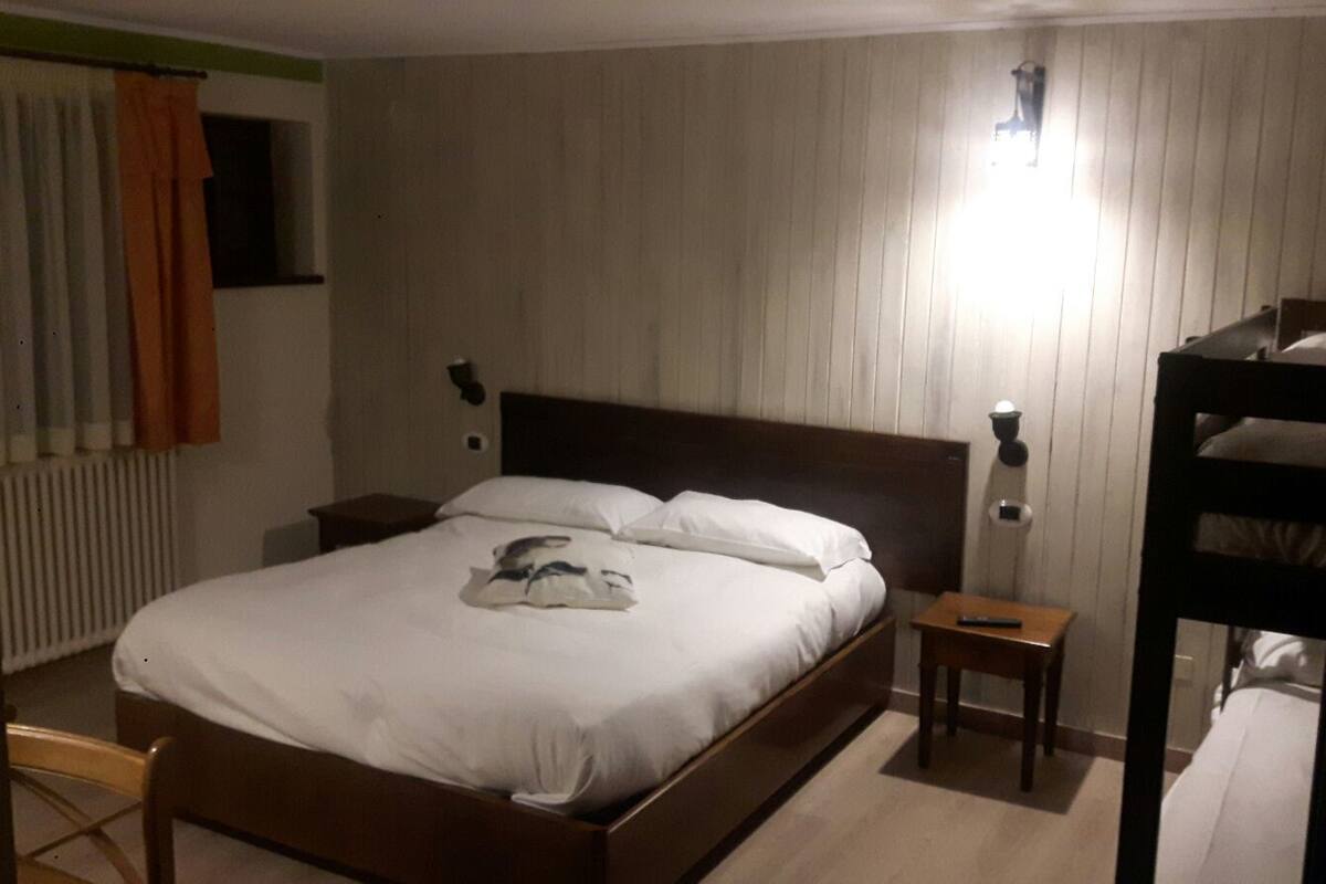 A single bed with a wooden headboard, a bedside table, a wall-mounted lamp, and a window with curtains.