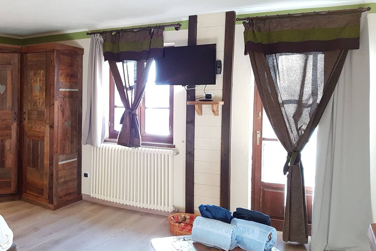 A cozy bedroom with a wooden headboard, a bed with white bedding, a nightstand, a dresser, and a TV mounted on the wall.