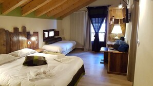 Una habitación con dos camas, cabecera de madera, un escritorio con lámpara y una ventana con cortinas.