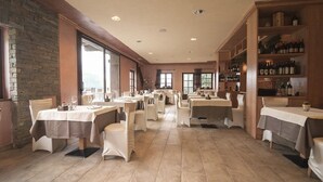 Un restaurante espacioso con múltiples mesas y sillas, una pared de piedra en un lado y una estantería para vinos en el otro.