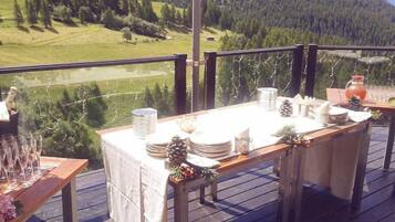 Eine Holzterrasse mit gedecktem Tisch, mit Blick auf eine gebirgige Landschaft.