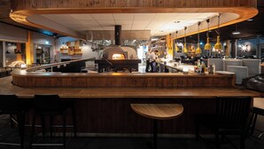A restaurant with a central wood-burning oven, a curved wooden bar, and hanging yellow pendant lights. - Bergshotellet (Jarvso)
