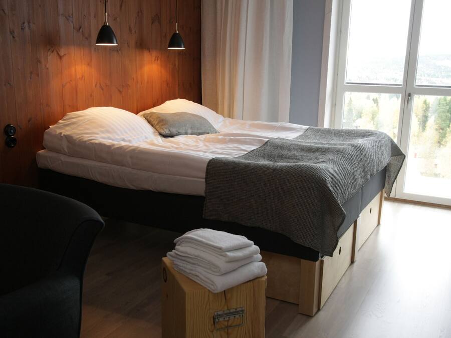 A bedroom with a bed, a chair, a window with a view, and a wooden wall.