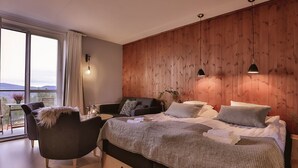A modern bedroom with a large bed, a sitting area with a chair, a small table, and a view of the outdoors. - Bergshotellet (Jarvso)