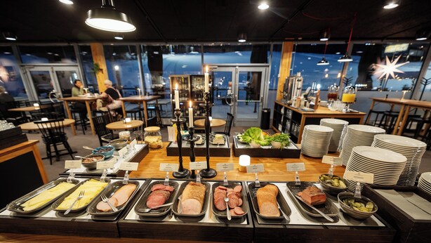 A buffet with various food options, including meats, cheeses, and salads, in a restaurant with a view of the city at night. - Bergshotellet (Jarvso)